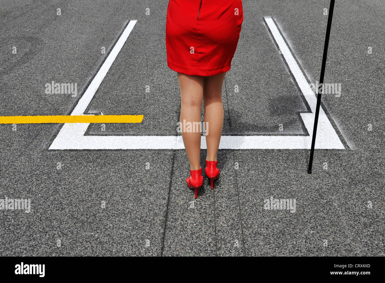 Raster-Mädchen im roten Kleid und roten hochhackigen Schuhe steht vor Start-Position für ein Formel-1-Rennwagen Stockfoto