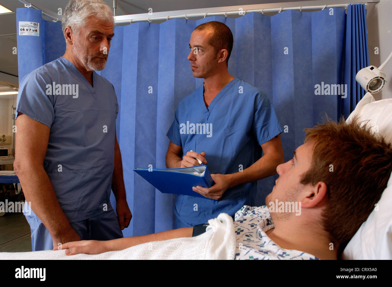 Ein bärtiger Chirurg und ein Mitglied seines chirurgischen Teams besuchen einen männlichen Patient im Bett nach einer Operation erholt. Stockfoto