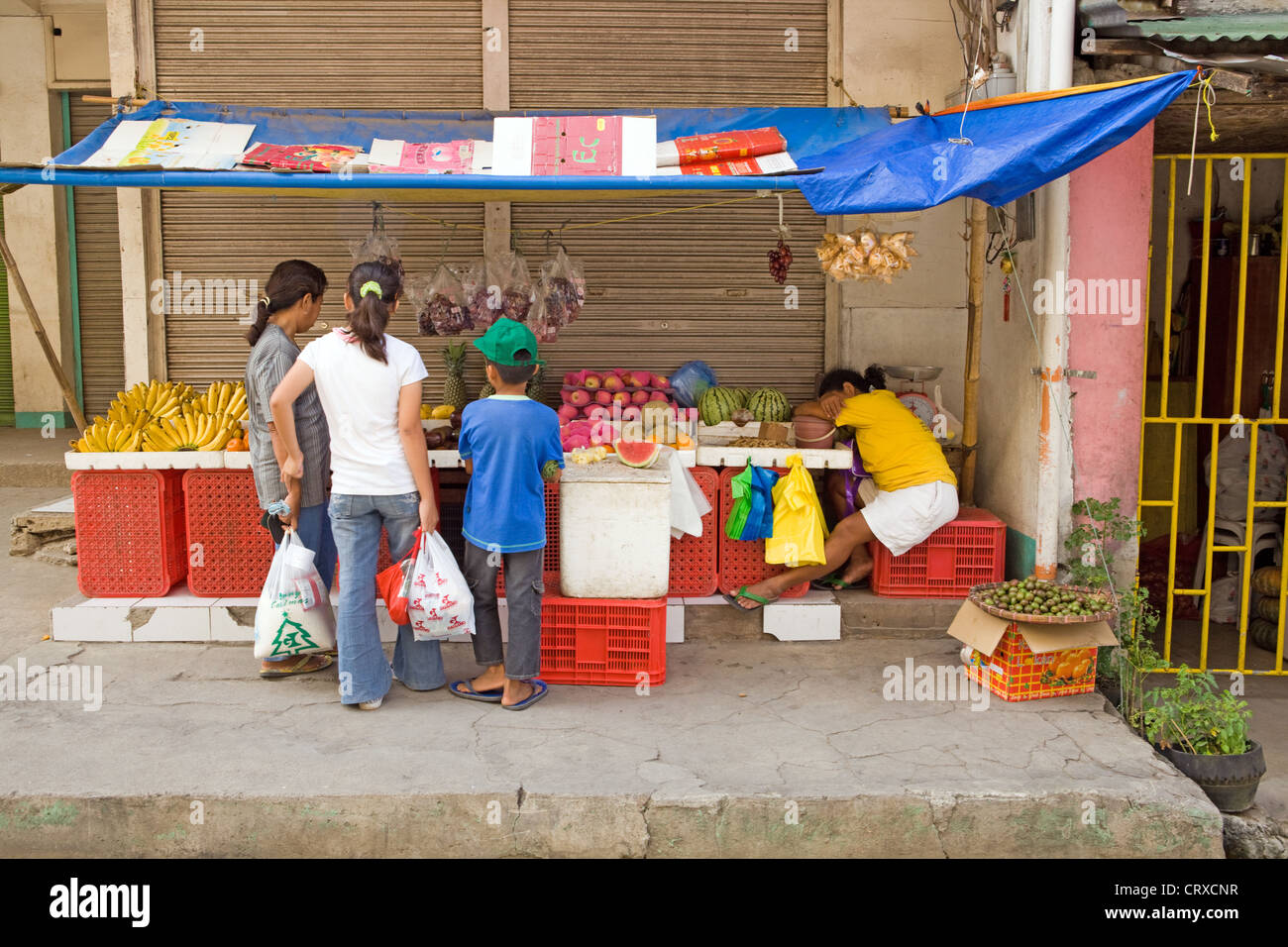Philippinische Familie Geschäfte für Obst am Stand ist ein verschlafenes Anbieter in Bogo Stadt, Insel Cebu, Philippinen. Stockfoto
