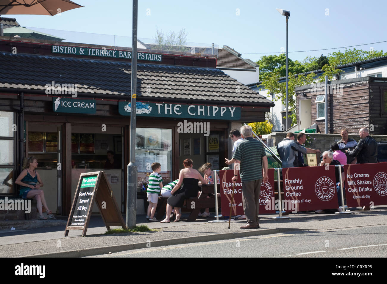 Ullapool Ross und Cromarty Schottland UK Touristen an Picknicktischen Essen Fish &amp; Chips draußen in der Sonne sitzen Stockfoto