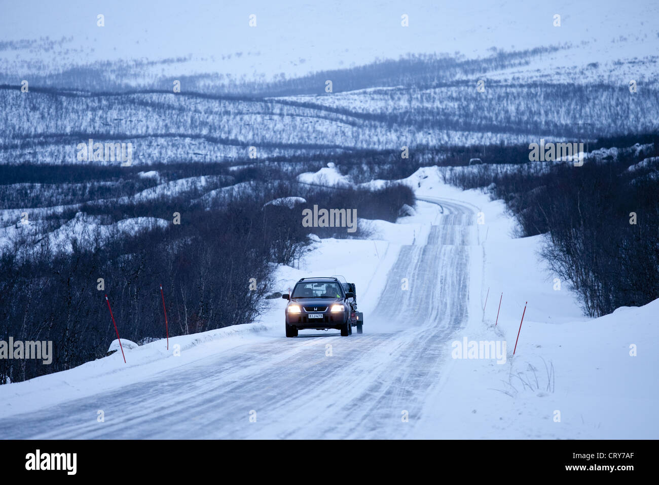 Auto mit Anhänger schleppen Schneemobil durch arktische Wildnis bei Einbruch der Dunkelheit von Kilpisjarvi auf dem Weg von Norwegen nach Finnland Stockfoto