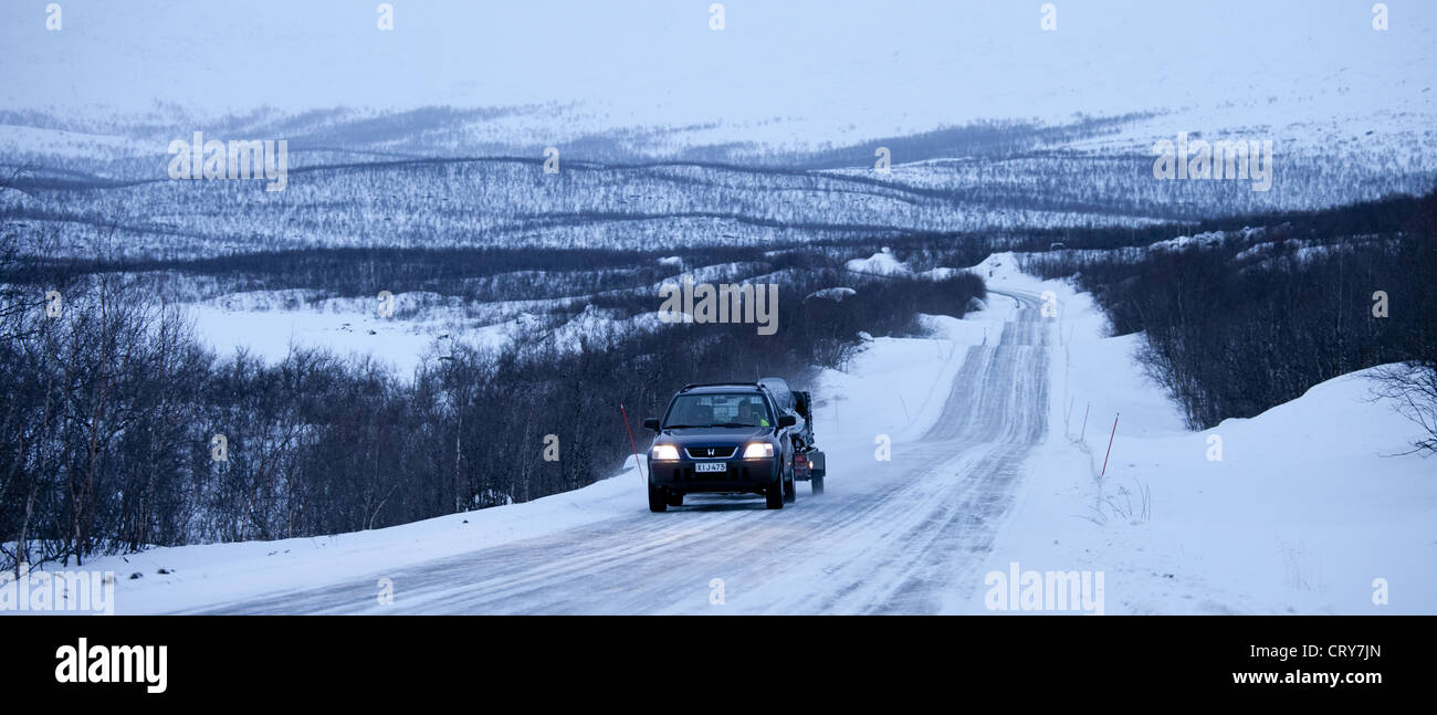 Auto mit Anhänger schleppen Schneemobil durch arktische Wildnis bei Einbruch der Dunkelheit von Kilpisjarvi auf dem Weg von Norwegen nach Finnland Stockfoto