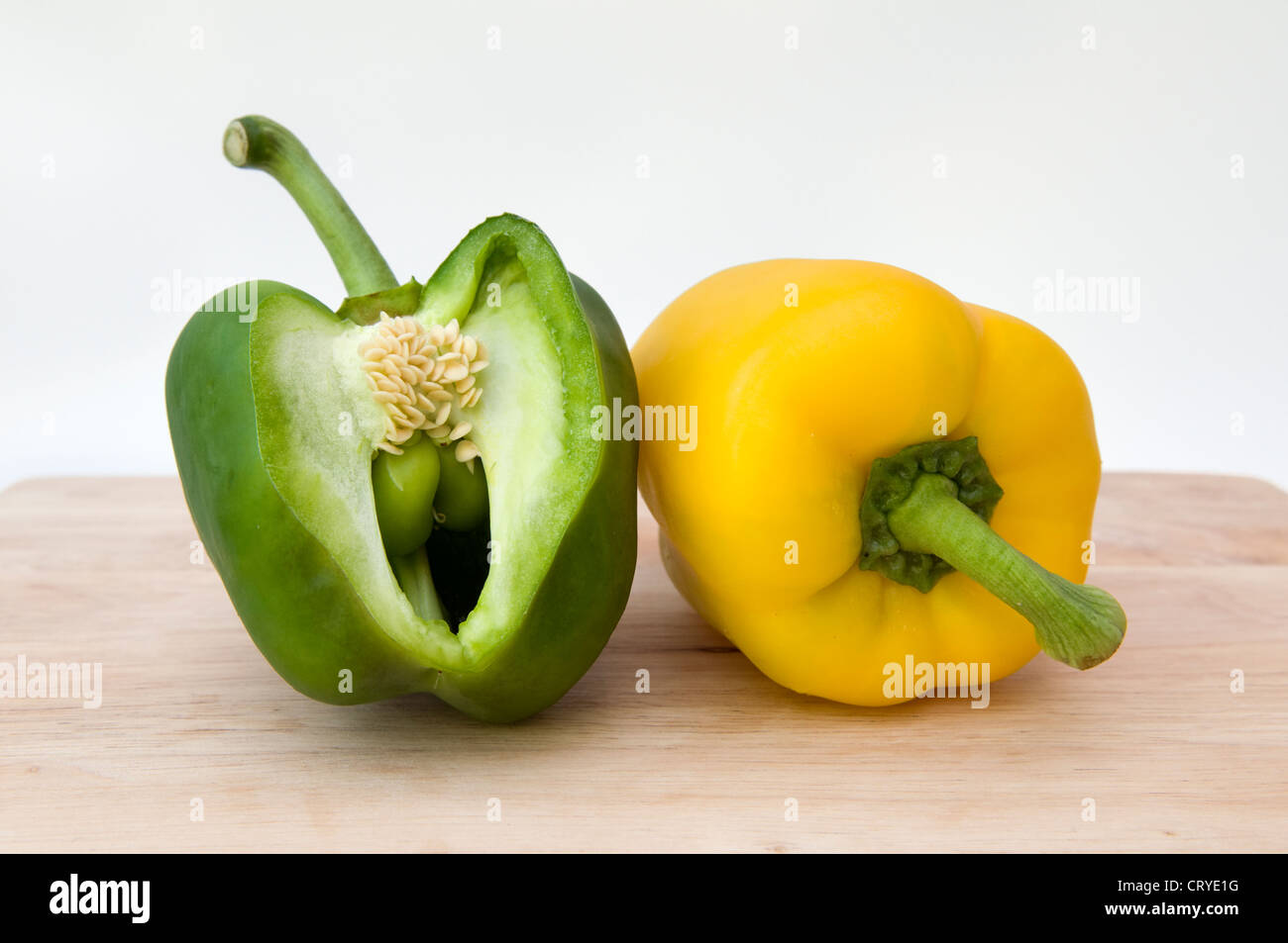 Nahaufnahme von grünen und gelben Paprika auf Schneidbrett aus Holz auf einem weißen Hintergrund Stockfoto