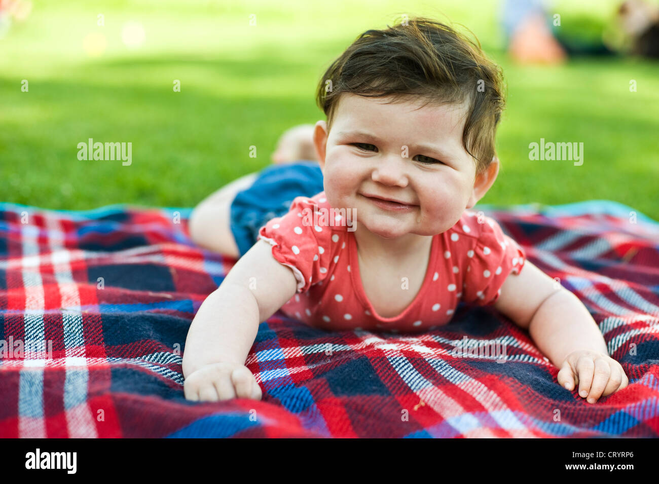 Glückliches Baby Girl (6 Monate alt) auf Picknick-Decke auf dem Rasen im Park mit Bauch Zeit Stockfoto