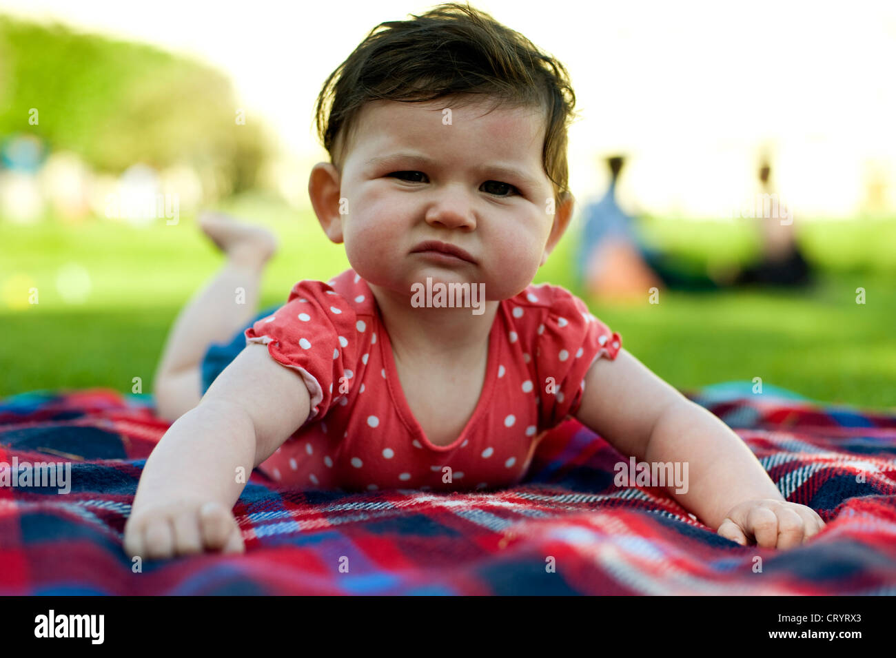 Babymädchen (6 Monate alt) auf Picknick-Matte auf dem Rasen im Park mit Bauch Zeit mit einem ernsten Blick auf ihrem Gesicht Stockfoto