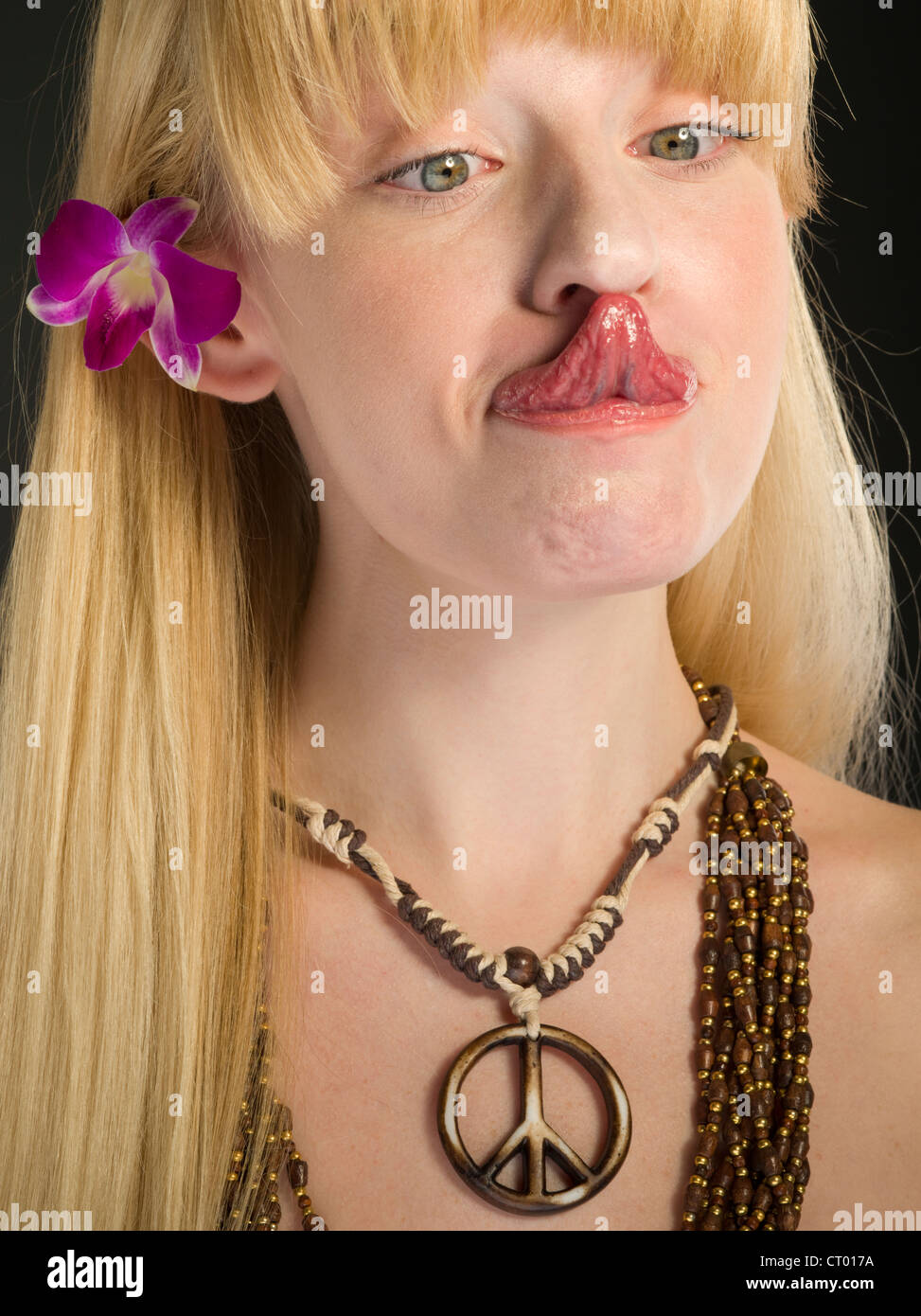 Junge Hippiemädchen mit Blume im Haar, ihre Zunge zu ihrer Nase zu berühren. Stockfoto