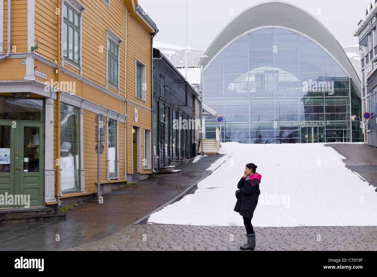 Einheimische Frau mit Handy im Straßenbild durch moderne Biblioteket Bibliothek in Tromsoya, Tromsø, Nordnorwegen Stockfoto