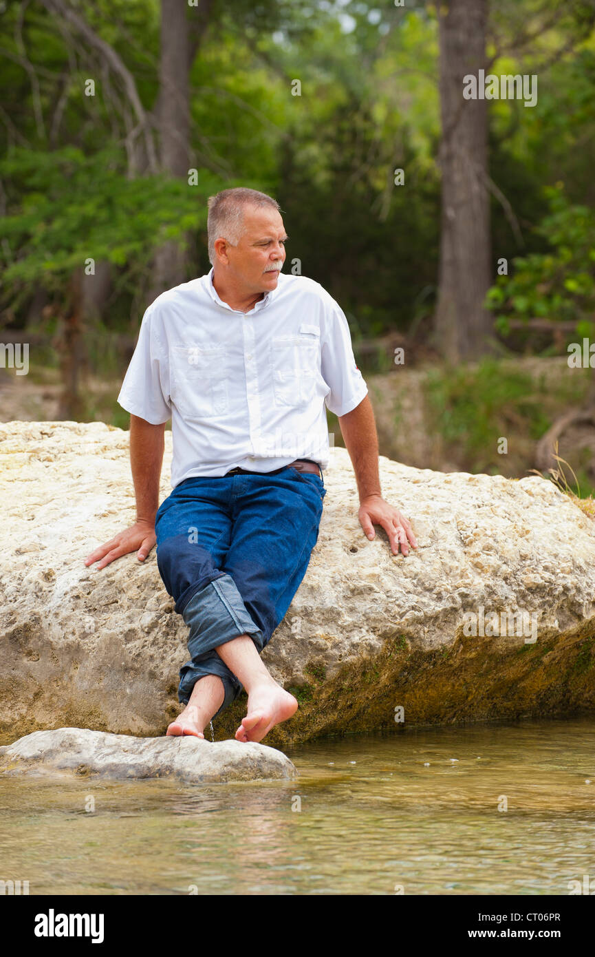 Porträt von einem reifen Mann in seinen 50er Jahre in einer natürlichen Umgebung mit den Füßen im Wasser der Frio River, Texas Stockfoto