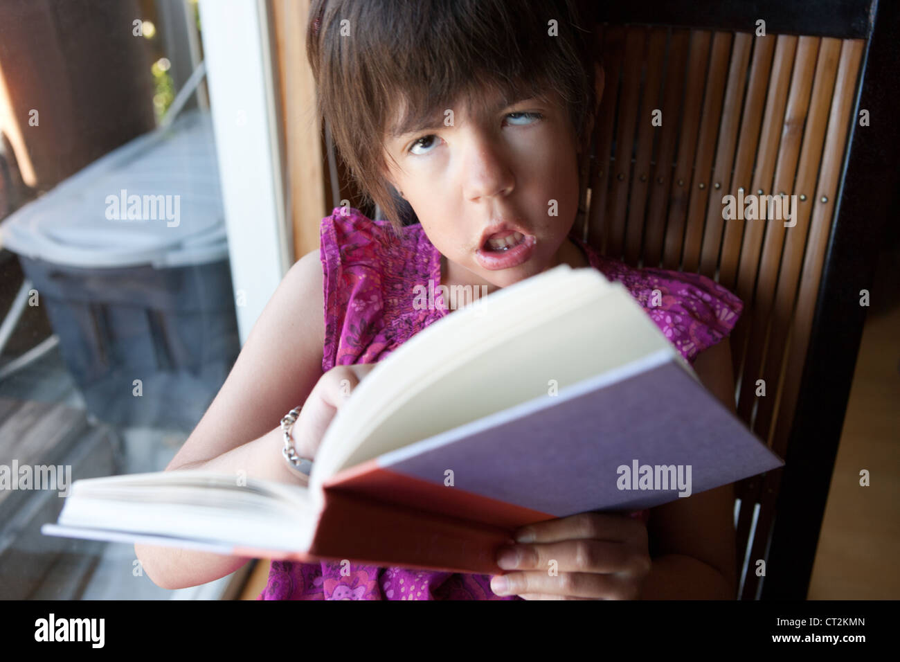 Sieben Jahre altes Mädchen mit Muskeldystrophie, die aus einem Buch nachschlagen ist sie zu Hause lesen. Stockfoto