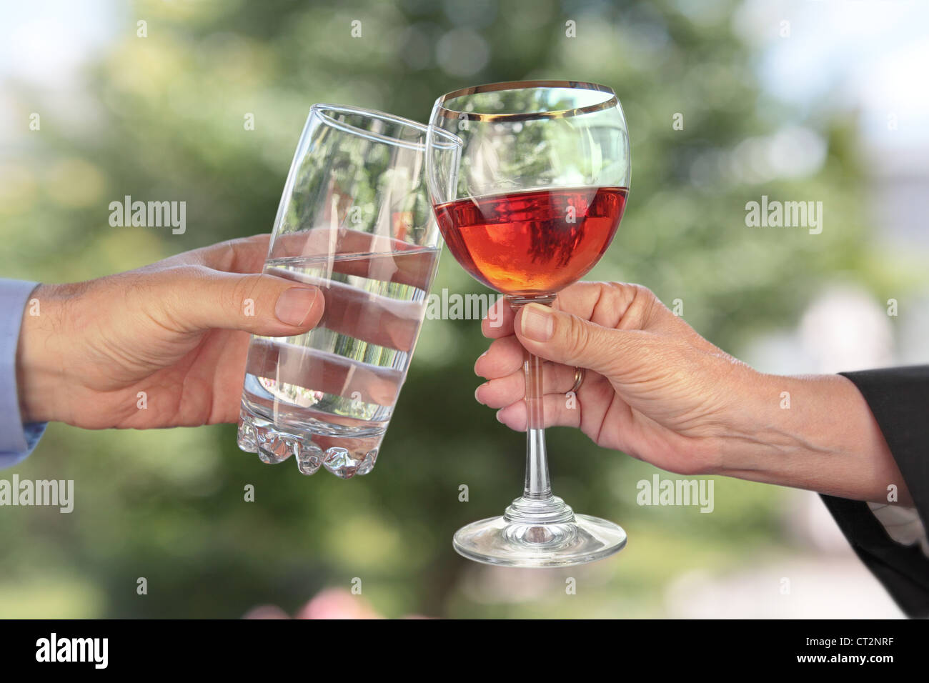 zwei Hände mit Gläser klirren; eine Hand hält ein Glas Wasser, die andere Hand hält ein Glas Alkohol Stockfoto