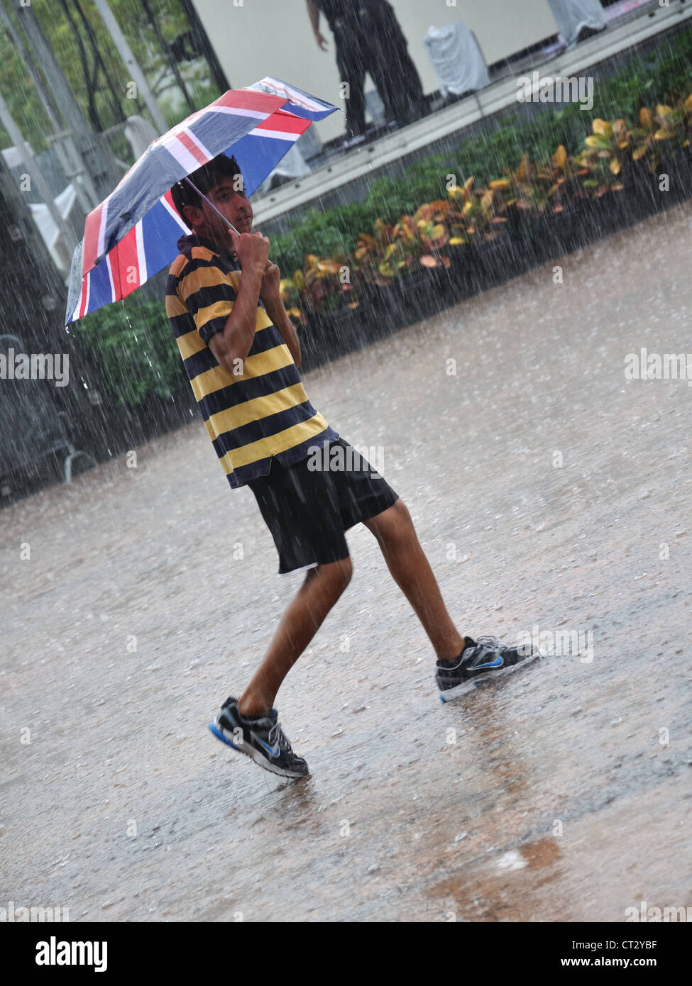 Junge mit britischer Flagge (Union Jack) Regenschirm in strömendem Regen bei einem Gewitter erwischt. Stockfoto