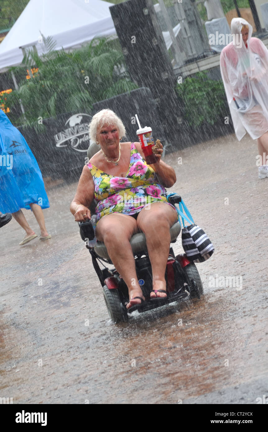 In strömendem Regen in einem Gewitter auf einen elektrischen Rollstuhl im Sommer Kleidung in einem Florida Theme Park, USA ausgesetzt. Stockfoto