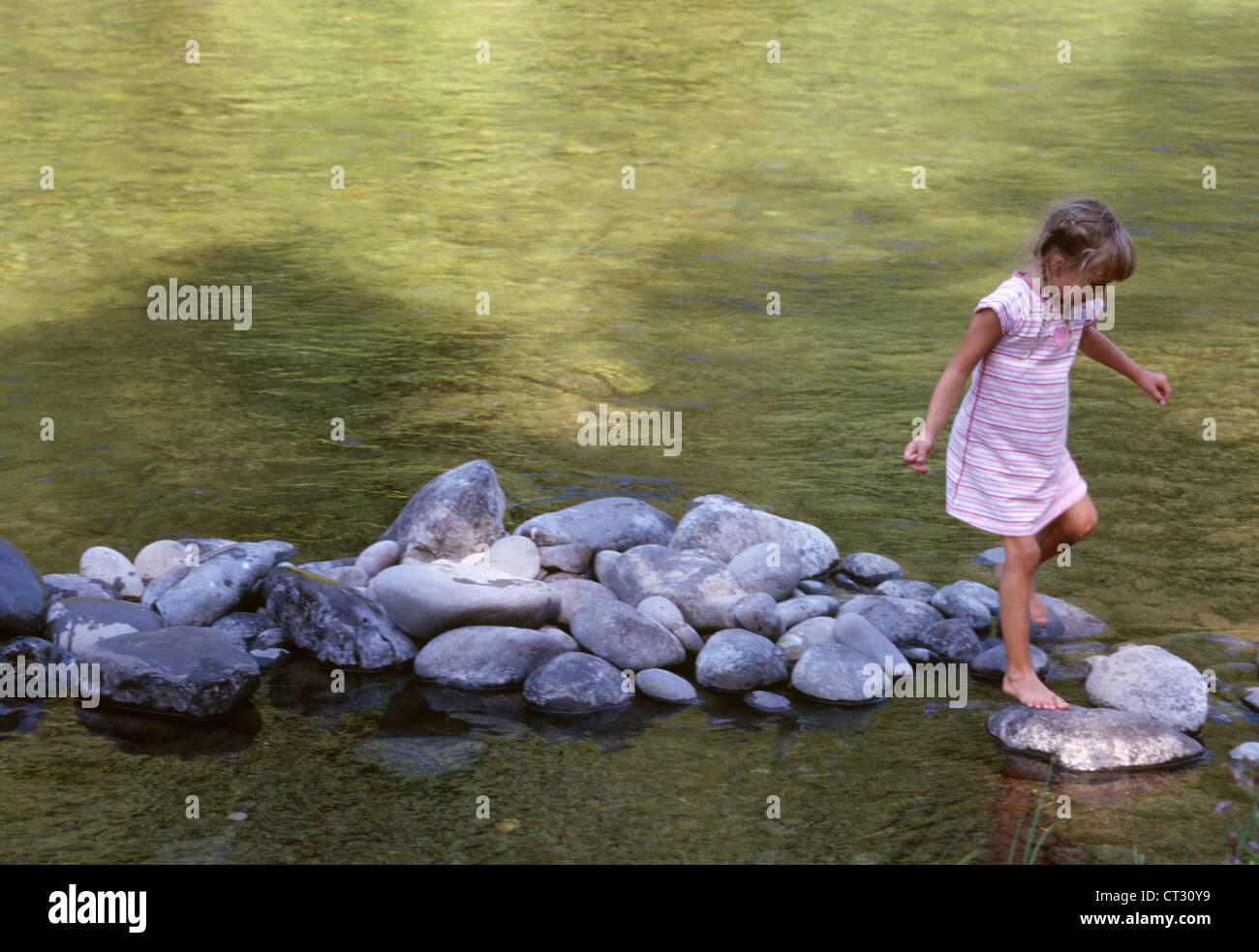 Ein junges Mädchen auf einige Flusssteine überspringen. Stockfoto