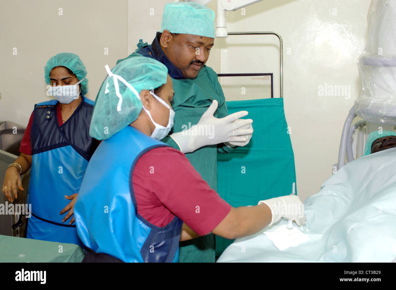 Ein Mitglied der kardiologische Versorgung Teams bereitet Ausrüstung während die Kardiologe seine OP-Handschuhe anzieht. Das Kleid wird über eine schützende blaue Schürze (verwendet, um die Wahrscheinlichkeit von schädlichen Wirkungen von Strahlung zu reduzieren) getragen. Stockfoto