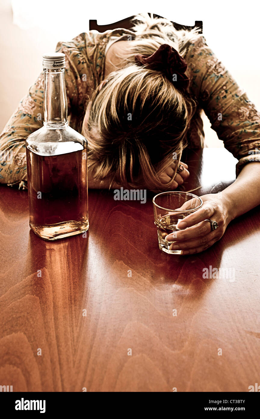 betrunken Frau mit halb leere Flasche und ein Glas Whisky Stockfoto