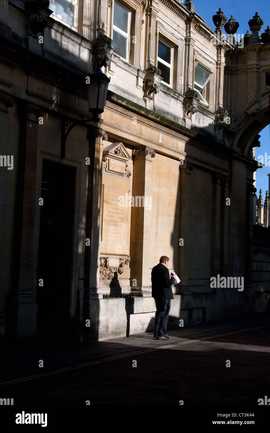 Ein Fußgänger ist gefangen in einem sonnendurchfluteten Patch gegen die kunstvoll geschnitzten Steinmauer der römischen Bäder: York Street, Bath, Großbritannien Stockfoto