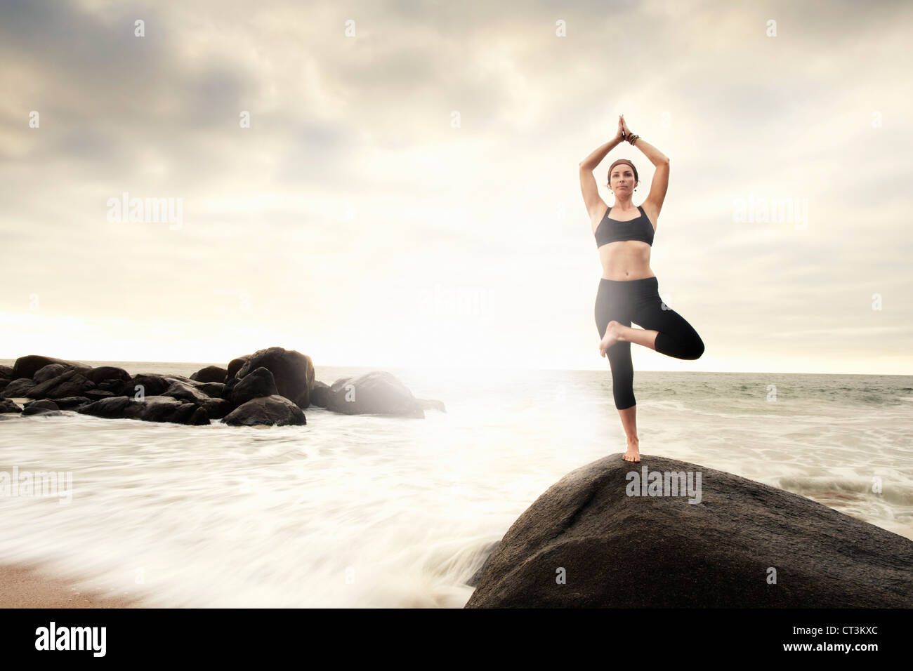 Frau praktizieren Yoga auf Felsen am Strand Stockfoto