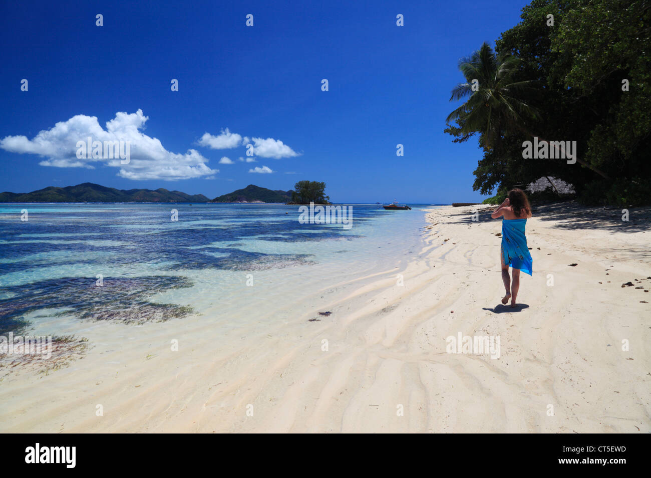 Frau in blau Sarong zu Fuß entlang des Strandes in der Nähe von Anse Source d ' Argent auf La Digue auf den Seychellen Stockfoto