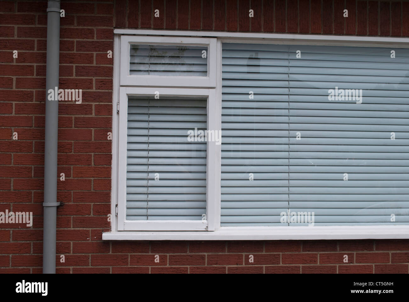 Weiße Fenster mit geschlossenen weiße Jalousie in roten Backsteinmauer mit grauen Kunststoff Regenrinne Stockfoto