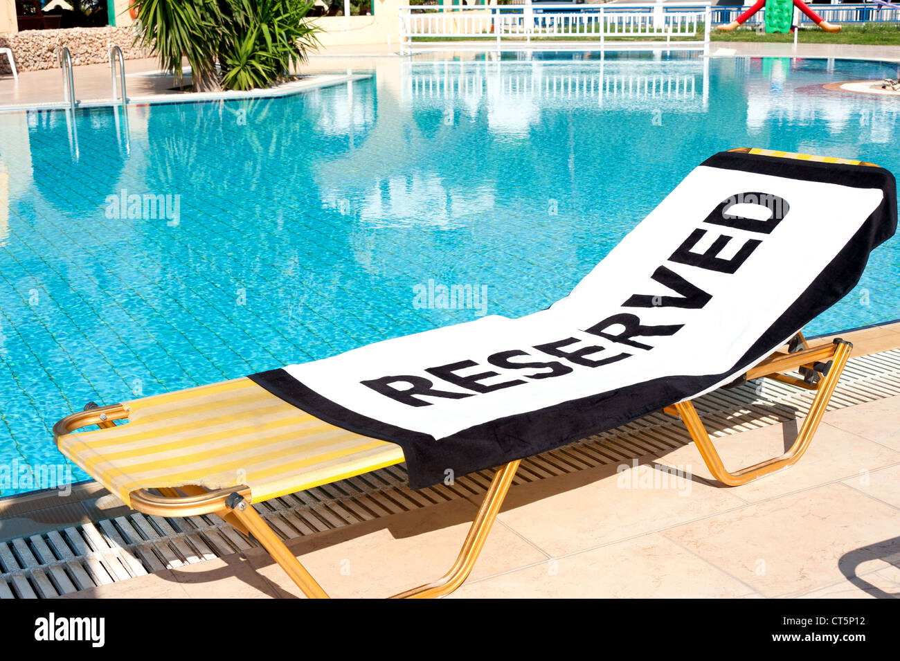 Ein Strandtuch mit dem Wort "Reserviert" zu verbreiten, auf einem Liegestuhl neben einem Schwimmbad Stockfoto