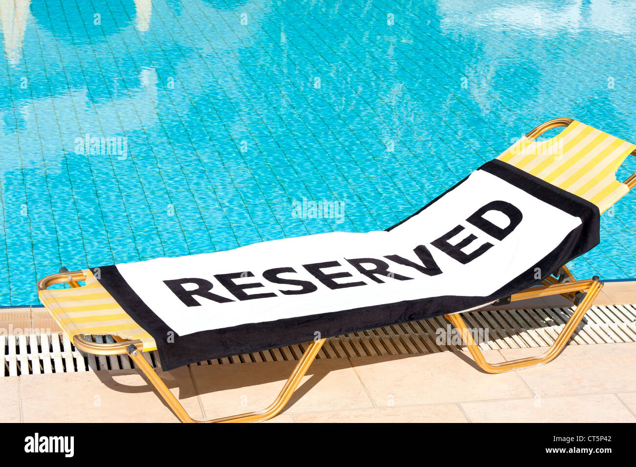 Ein Strandtuch mit dem Wort "Reserviert" zu verbreiten, auf einem Liegestuhl neben einem Schwimmbad Stockfoto