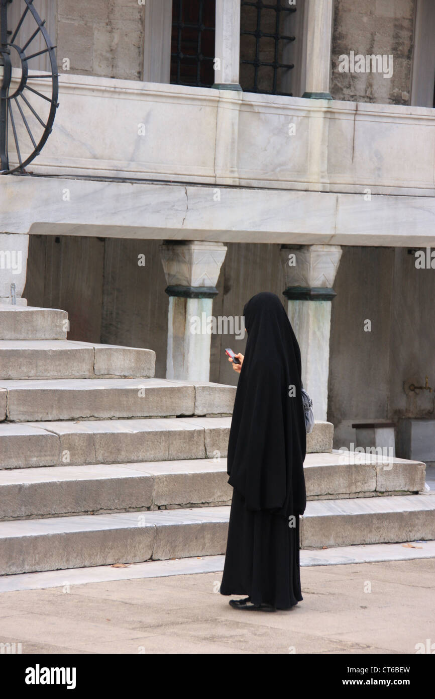Die muslimische Frau im schwarzen Tschador mit Handy, Innenhof des Sultan Ahmed Mosque, Sultanahmet, Istanbul, Türkei Stockfoto
