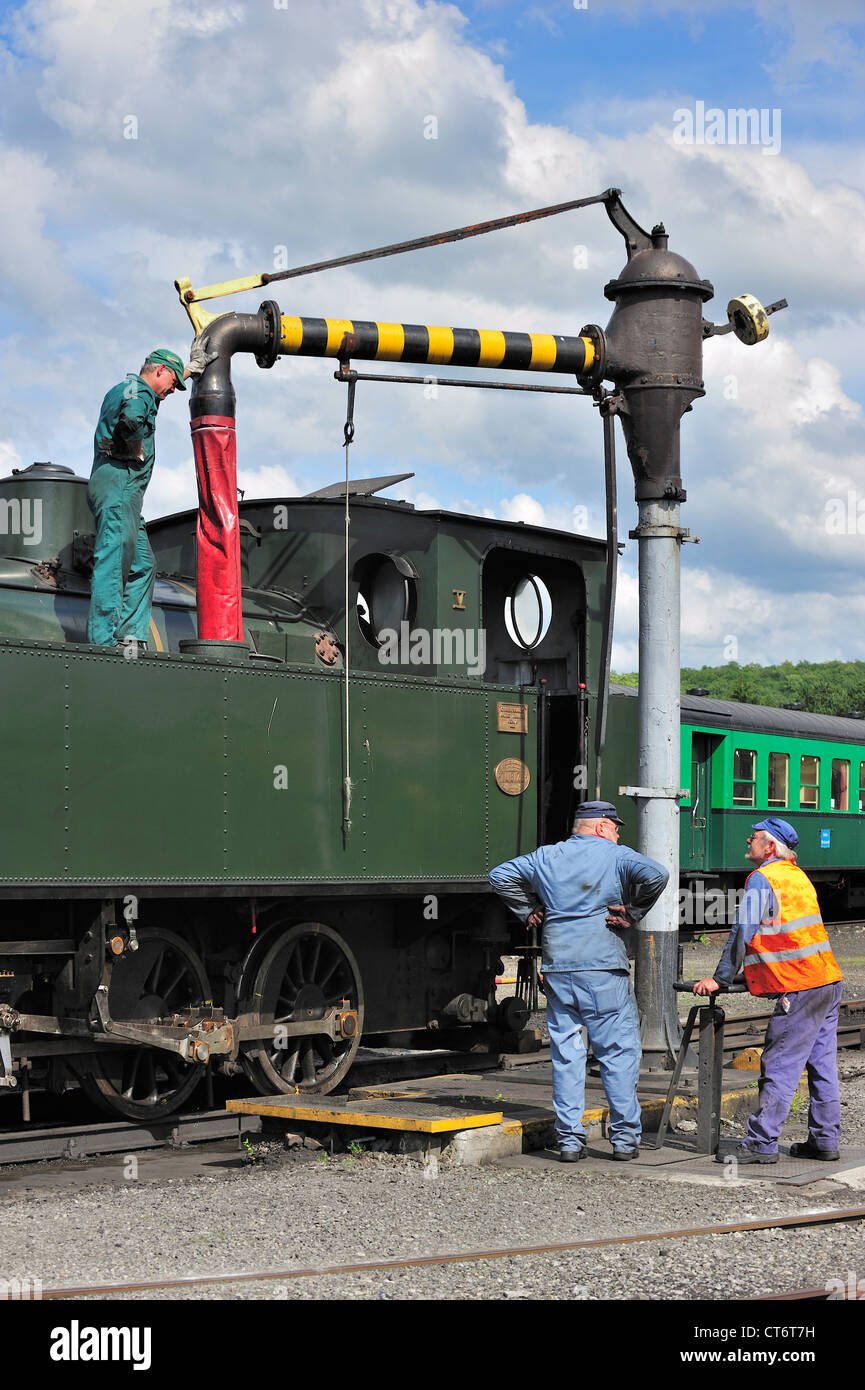 Lokführer und Crew füllen Kessel der Dampflok von Wasserkran im Depot des Trois Vallées in Mariembourg, Belgien Stockfoto