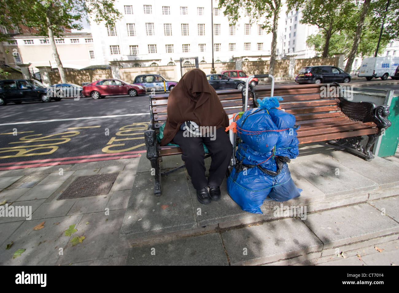 Ein Obdachloser sitzt auf einer Bank am Embankment in London, Großbritannien, umgeben von seinem hab und gut und sein Gesicht ist aus Privatsphäre bedeckt. Die Szene spiegelt die raue Realität des Lebens auf den Straßen wider, vor dem Hintergrund eines der berühmtesten Orte am Fluss der Stadt. Gebündelte Besitztümer und Kleidungsschichten sprechen von dem täglichen Kampf um Unterkunft und würde und heben den Kontrast zwischen städtischem Wohlstand und sichtbarer Obdachlosigkeit in der Hauptstadt hervor. Stockfoto Ein Obdachloser sitzt auf einer Bank am Embankment in London, Großbritannien, umgeben von seinem hab und gut und sein Gesicht ist aus Privatsphäre bedeckt. Die Szene spiegelt die raue Realität des Lebens auf den Straßen wider, vor dem Hintergrund eines der berühmtesten Orte am Fluss der Stadt. Gebündelte Besitztümer und Kleidungsschichten sprechen von dem täglichen Kampf um Unterkunft und würde und heben den Kontrast zwischen städtischem Wohlstand und sichtbarer Obdachlosigkeit in der Hauptstadt hervor. Stockfoto