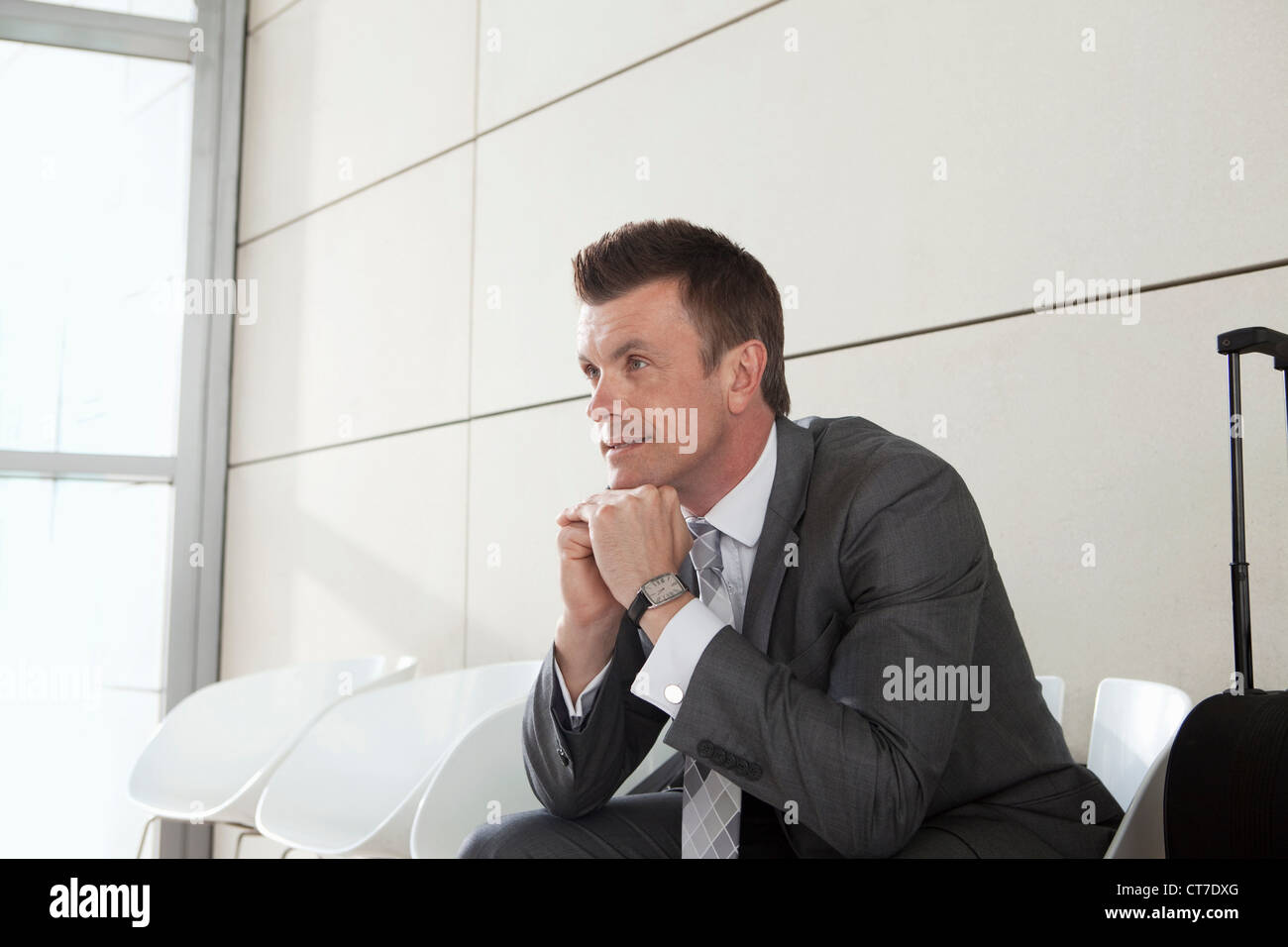 Geschäftsmann wartet mit Gepäck, hand aufs Kinn Stockfoto