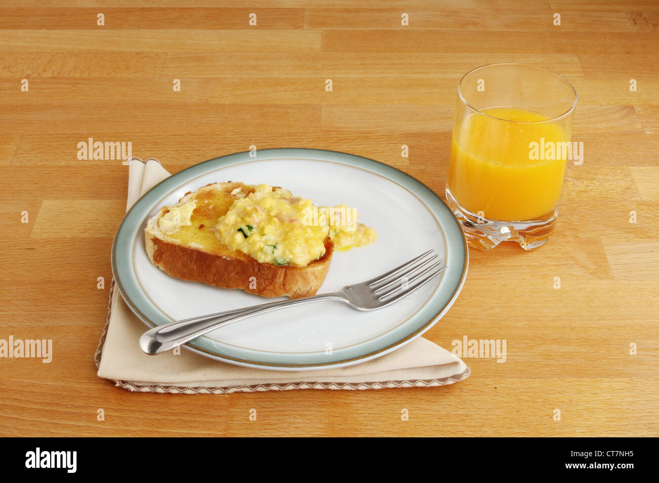 Ein einfaches Frühstück mit Rührei auf Toast und ein Glas Orangensaft auf einem Holztisch Stockfoto