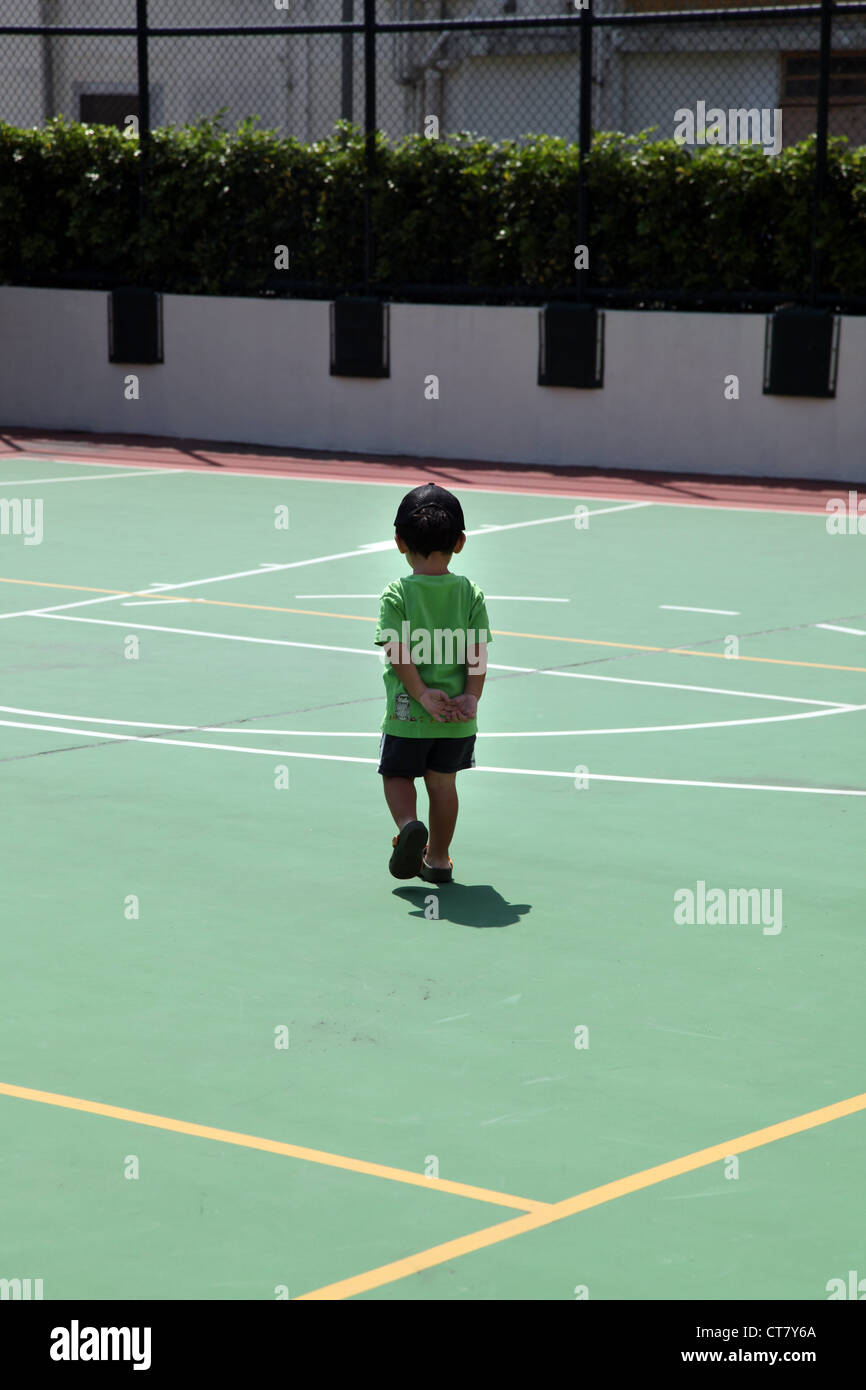 Es ist ein Foto eines kleinen Jungen alleine auf einem Korb Ball Spielplatz spielen. Der Boden ist grün beschichtet. I-sonnig Stockfoto