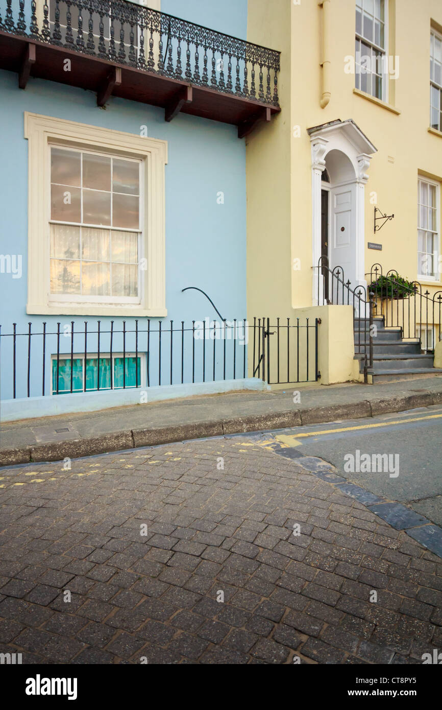 Reflexion des Sonnenuntergangs im Schiebefenster von einem blau lackierten Regency Haus mit Balkon neben ein gelbes Haus mit Doorcase in Tenby. Stockfoto