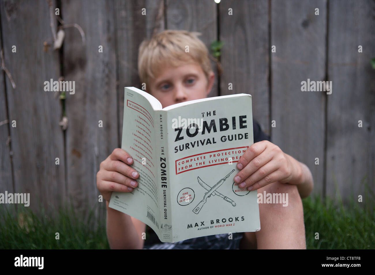 Neun Jahre alten Jungen beim Zombie Survival Guide lesen im Freien. Stockfoto