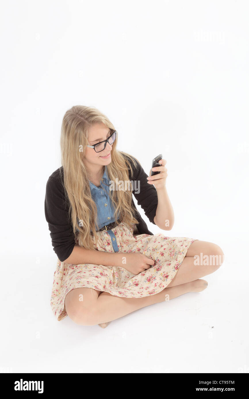 Junge hübsche Frau mit Brille, sitzen cross legged Blick auf ihr Handy. Isolierte Hintergrund. Stockfoto