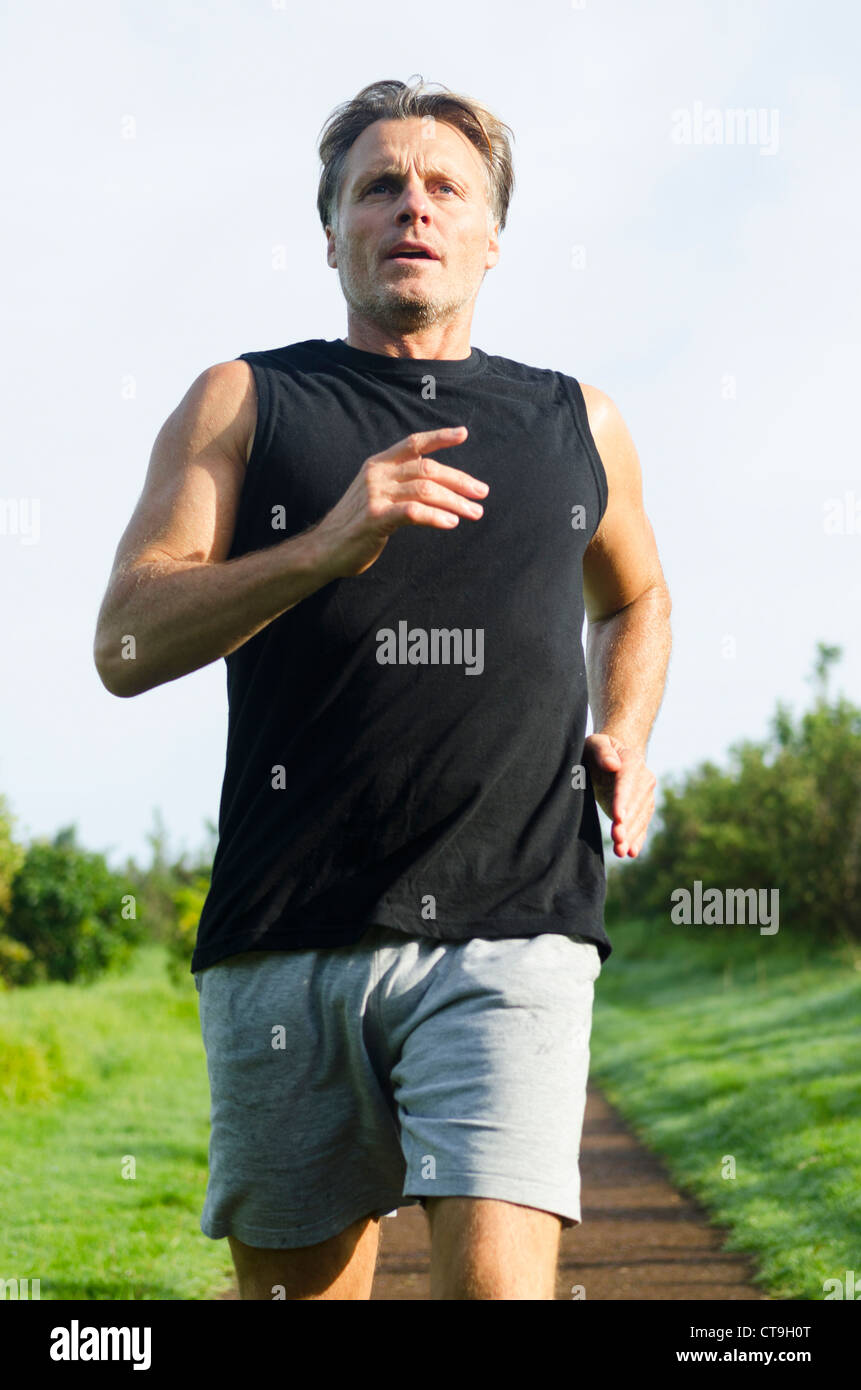 Ein Mann läuft entlang eines Weges tragen einen schwarzen Tank-Top und graue Shorts. Stockfoto
