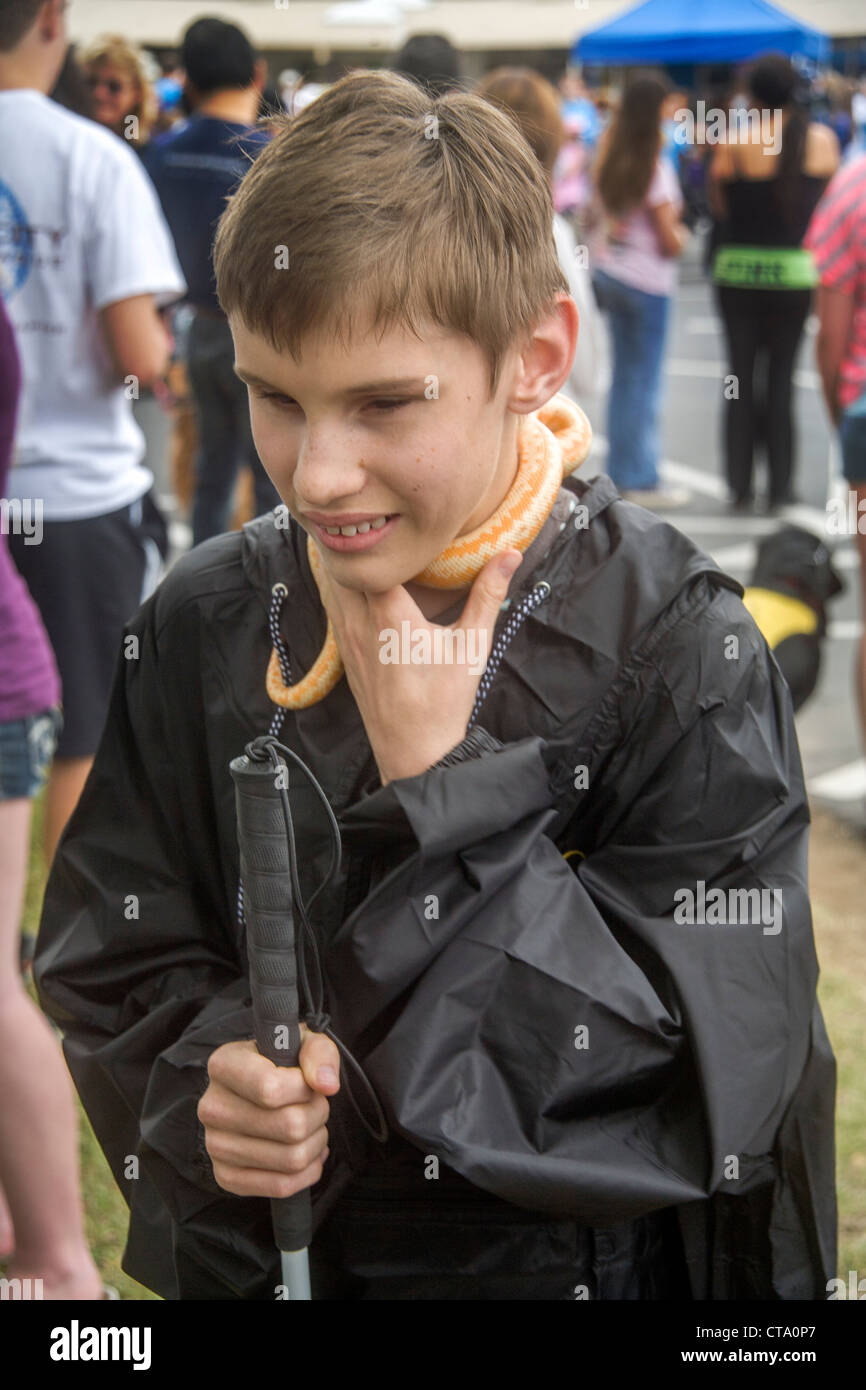 Ein blinder Junge fühlt sich eine Schlange um den Hals an einer Spendenaktion für Kinder mit Sehstörungen drapiert. Stockfoto