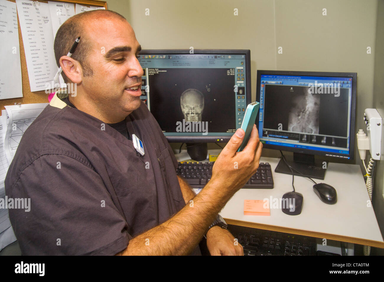 Ein Radiologe diktiert in ein iPhone an einen digitalen Arbeitsplatz in einer Klinik in Laguna Hills, CA. Beachten Sie die Monitore im Hintergrund. Stockfoto