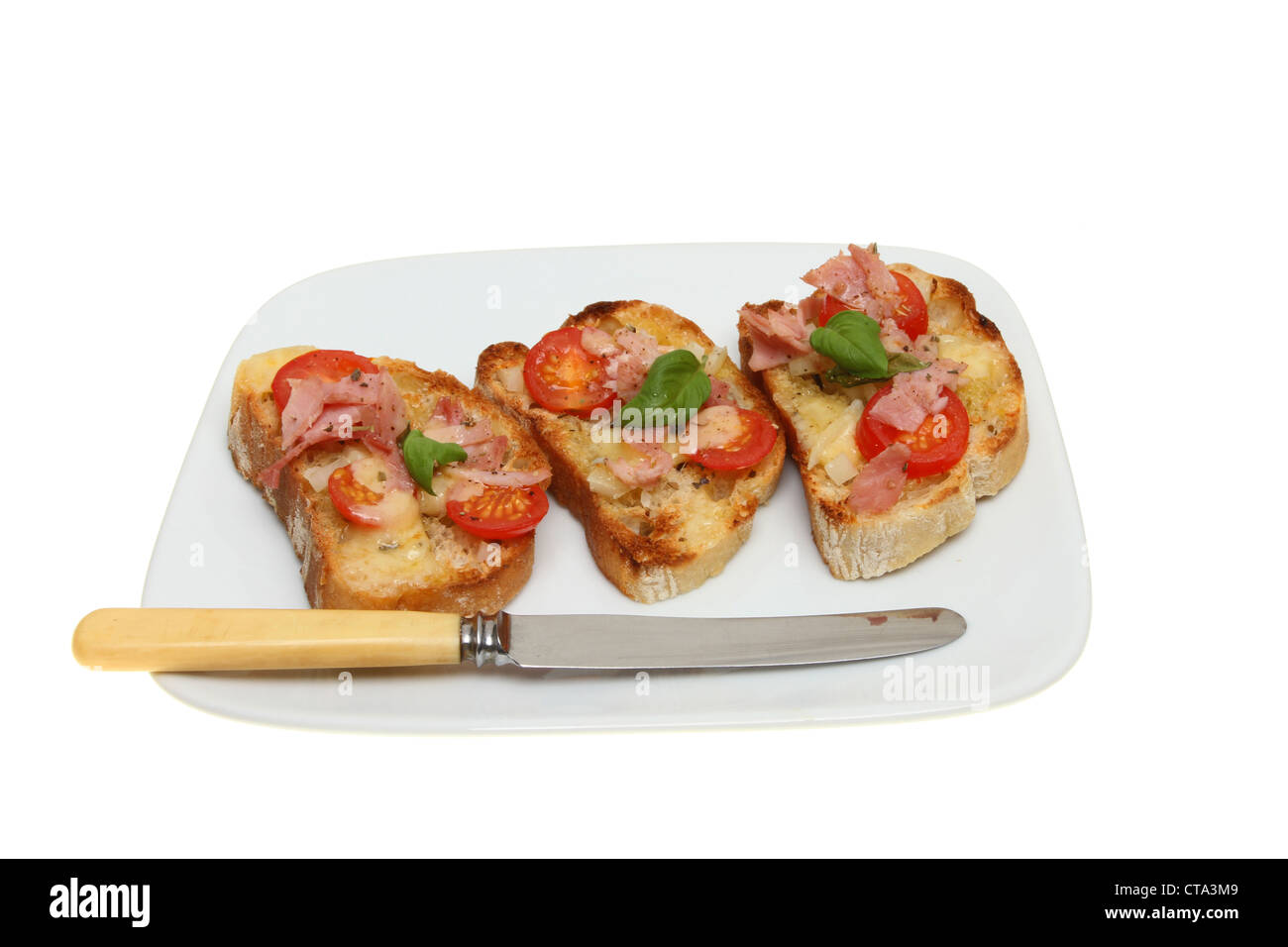 Geröstete Ciabata Brot mit Käse, Tomaten, Schinken und Basilikum auf einem Teller mit einem Messer isoliert gegen weiß Stockfoto