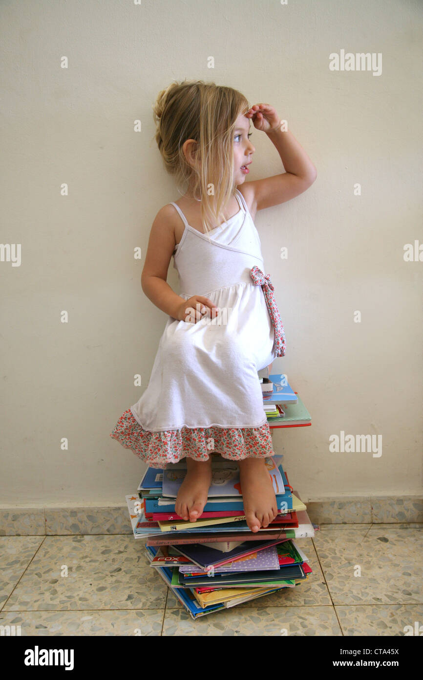 Mädchen von drei sitzt auf einem Stapel Bücher schaut nach rechts Stockfoto