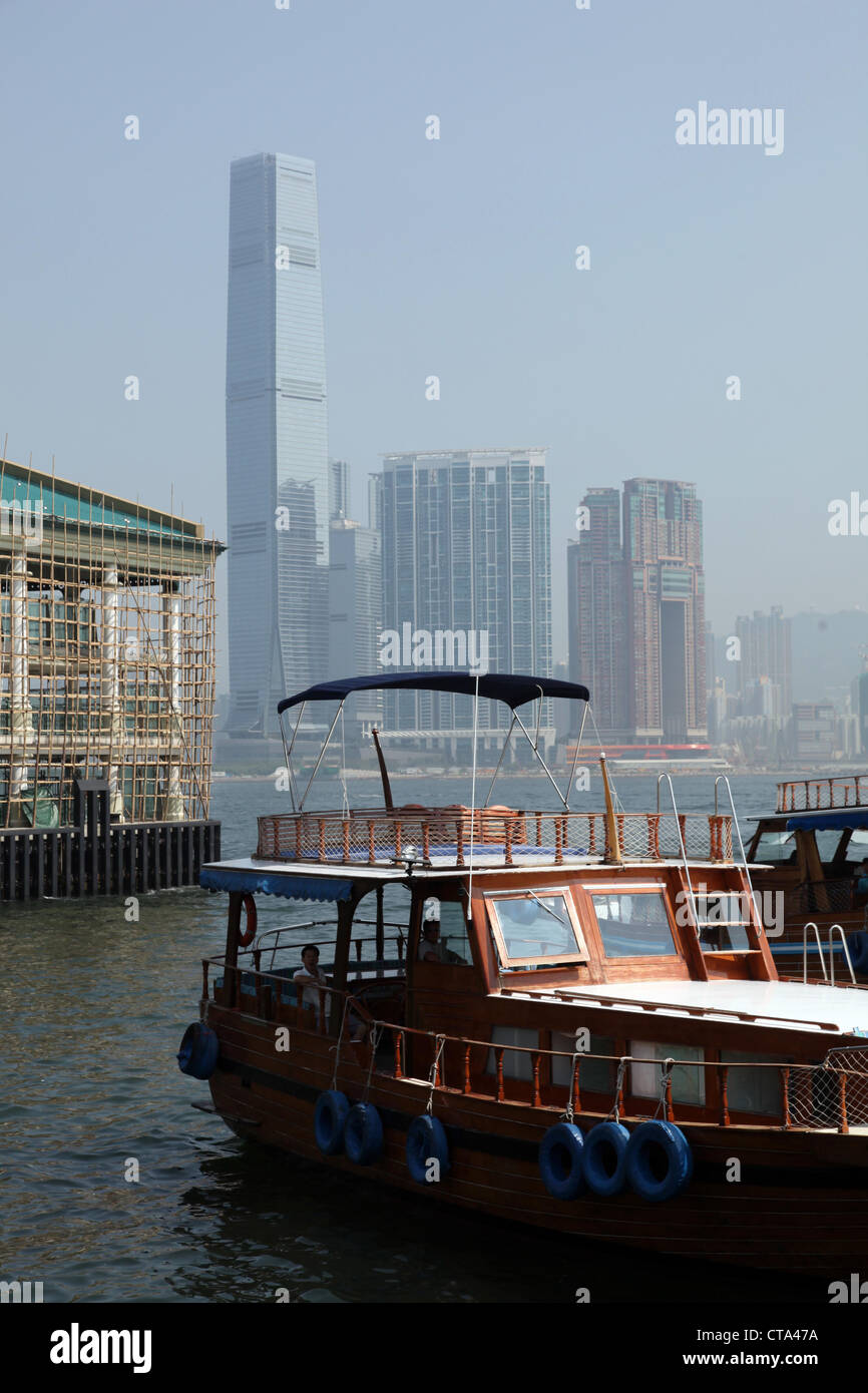 Es ist ein Foto von einem Boot in Hong Kong im Victoria Harbour. Wir sehen die Stadt in He Hintergrund. Wir sehen auch eine Holz Dschunke Stockfoto