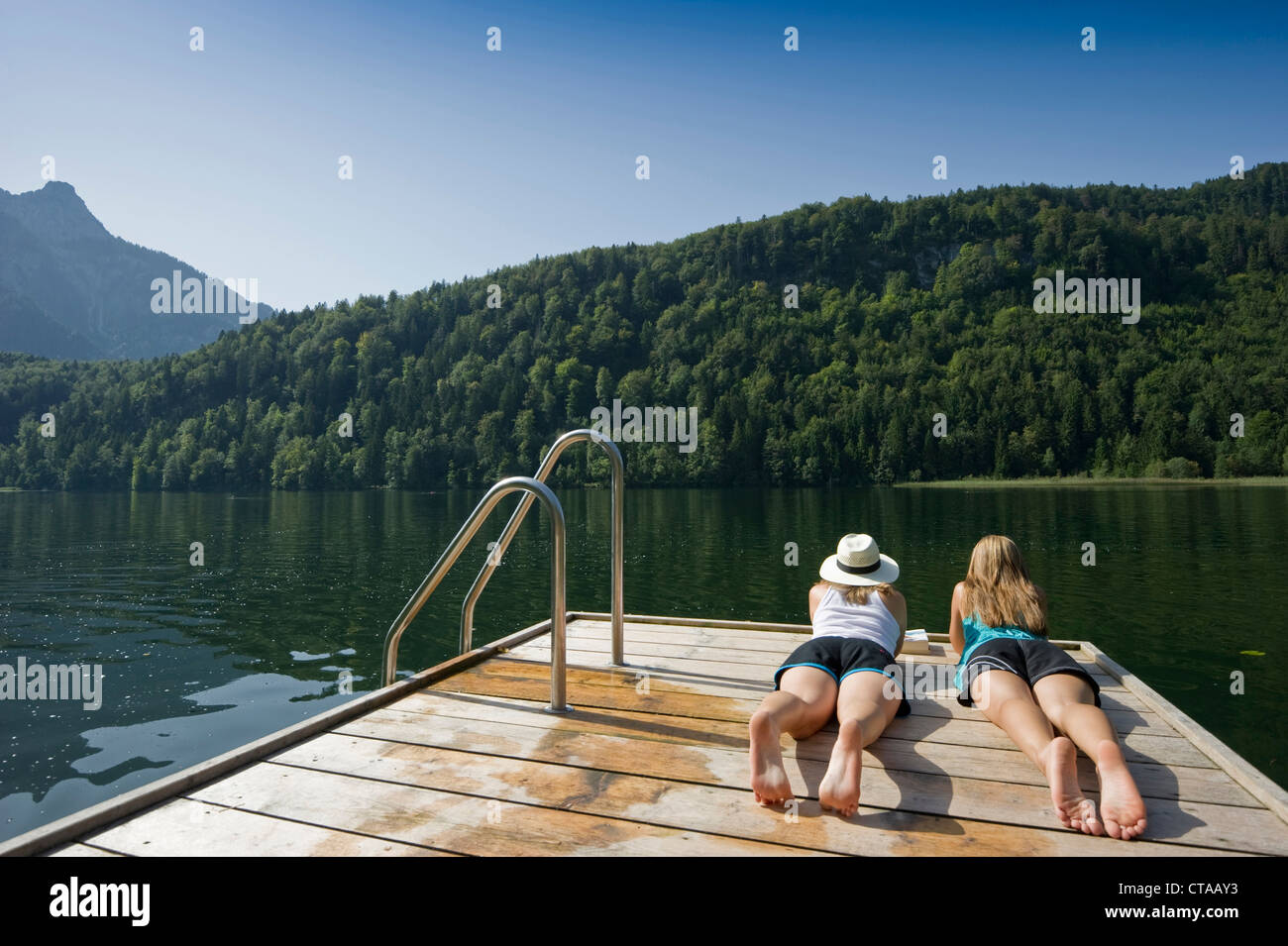 Zwei Mädchen im Teenageralter liegend auf einem Steg am See Schwansee, Schwangau, Allgäu, Bayern, Deutschland Stockfoto