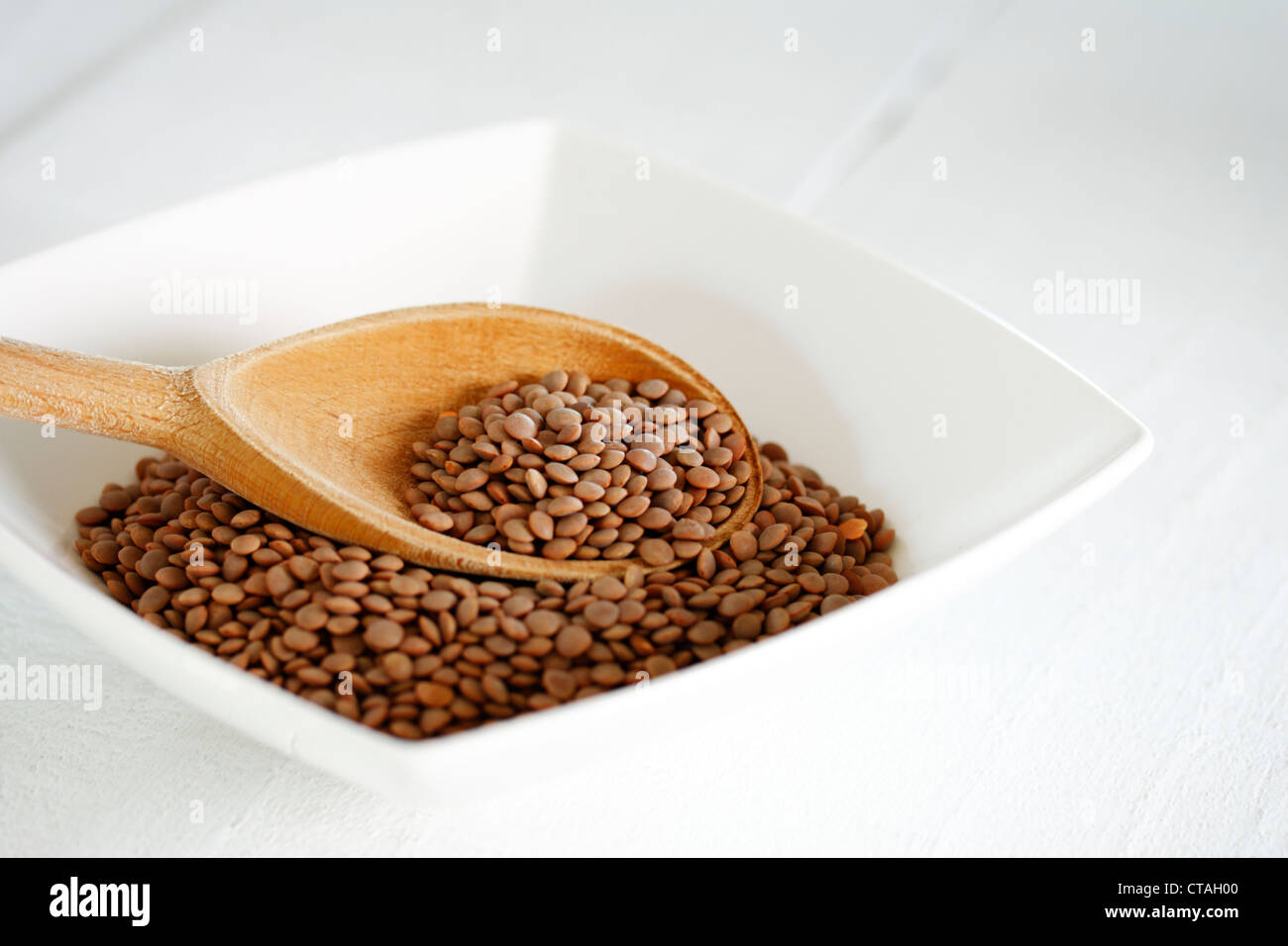 Eine Schüssel mit braune Linsen (Lens Culinaris) mit einem Holzlöffel Stockfoto
