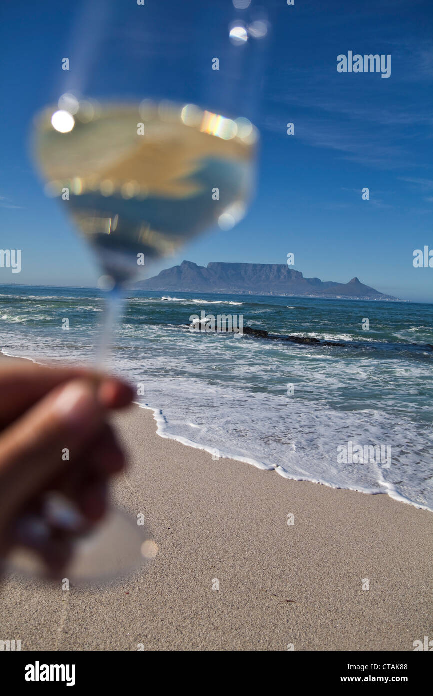 Hand hält ein Glas Weißwein am Bloubergstrand mit dem Tafelberg im Hintergrund, Western Cape, South Africa, RSA, Afri Stockfoto