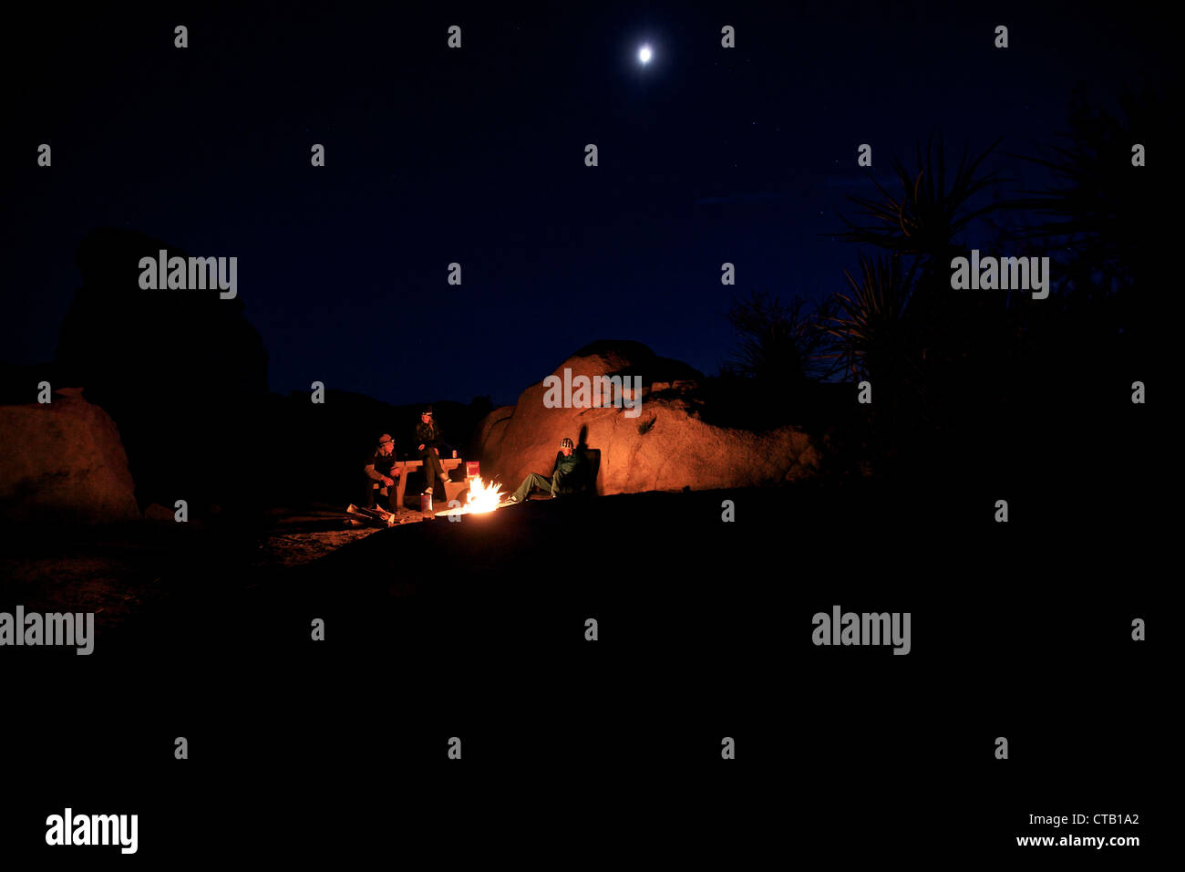 Drei Personen zusammen sitzen um ein Lagerfeuer, Joshua Tree Nationalpark, Kalifornien, USA Stockfoto