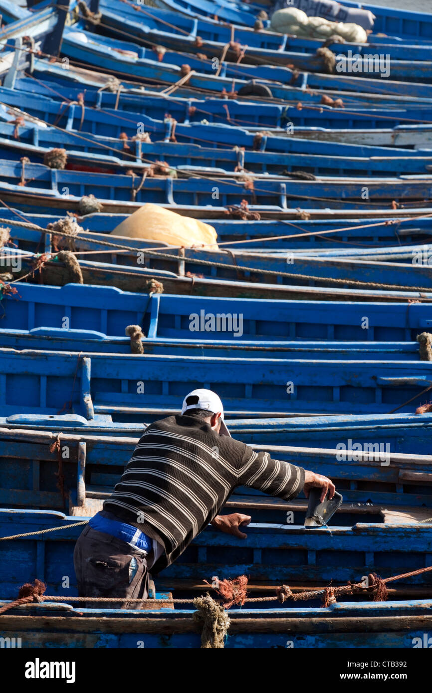 Ein Fischer arbeitet an einem traditionellen blauen Fischerboot im Hafen, Essaouira, Marokko Afrika Stockfoto