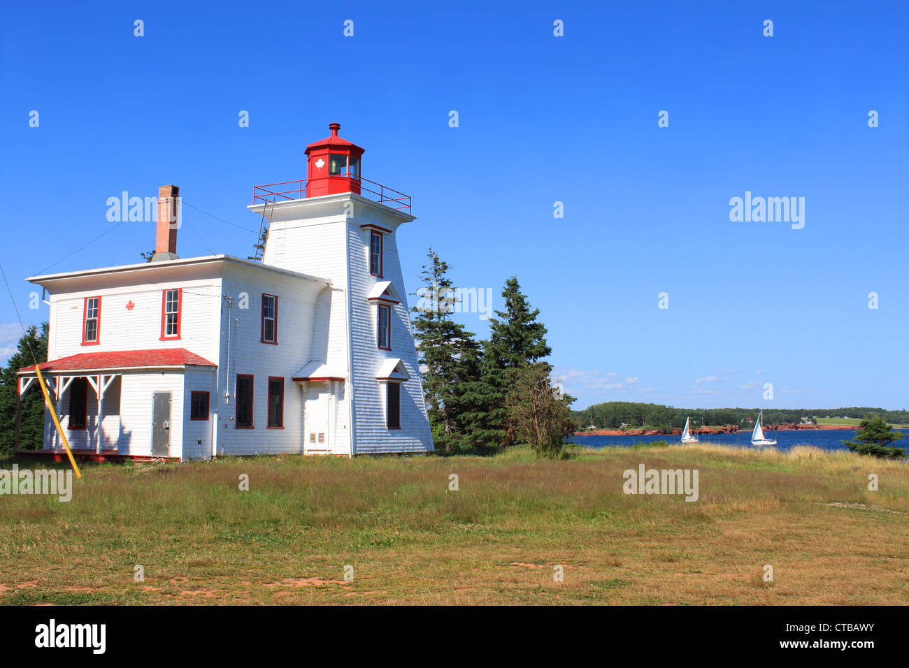 Leuchtturm am Rocky Point, Prince Edward Island, Kanada unter blauem Himmel mit Segelbooten im Hintergrund Stockfoto