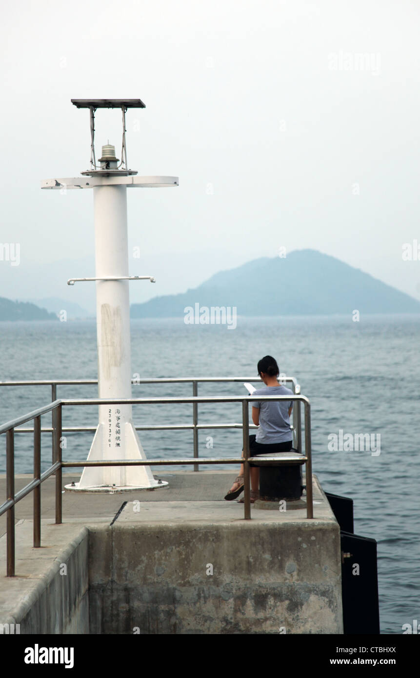 Es ' ein Foto von dem Hafen Doc oder Plattform nahe dem Meer Ozean. Wir sehen den Rücken jemanden sitzen auf Poller mit Blick aufs Meer Stockfoto