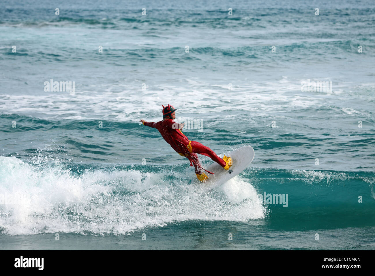 Bärtiger Mann Surfen eine Welle rot Superhelden-Kostüm tragen. Stockfoto