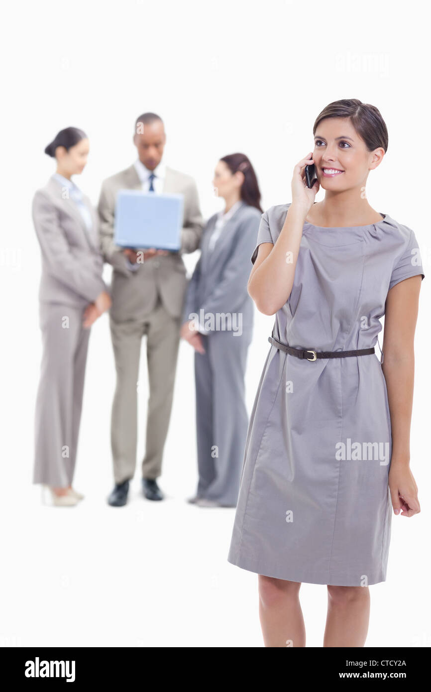 Geschäftsfrau Lächeln am Telefon mit einem Arm auf ihren Körper und die Kollegen im Hintergrund Stockfoto
