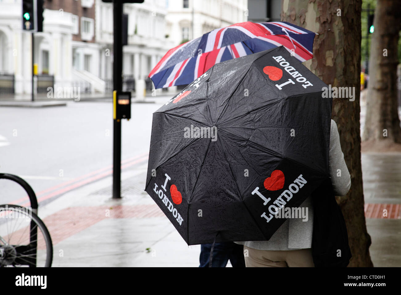 Regen in London, Touristen mit Regenschirmen auf einer Straße im Sommer, England, Großbritannien Stockfoto